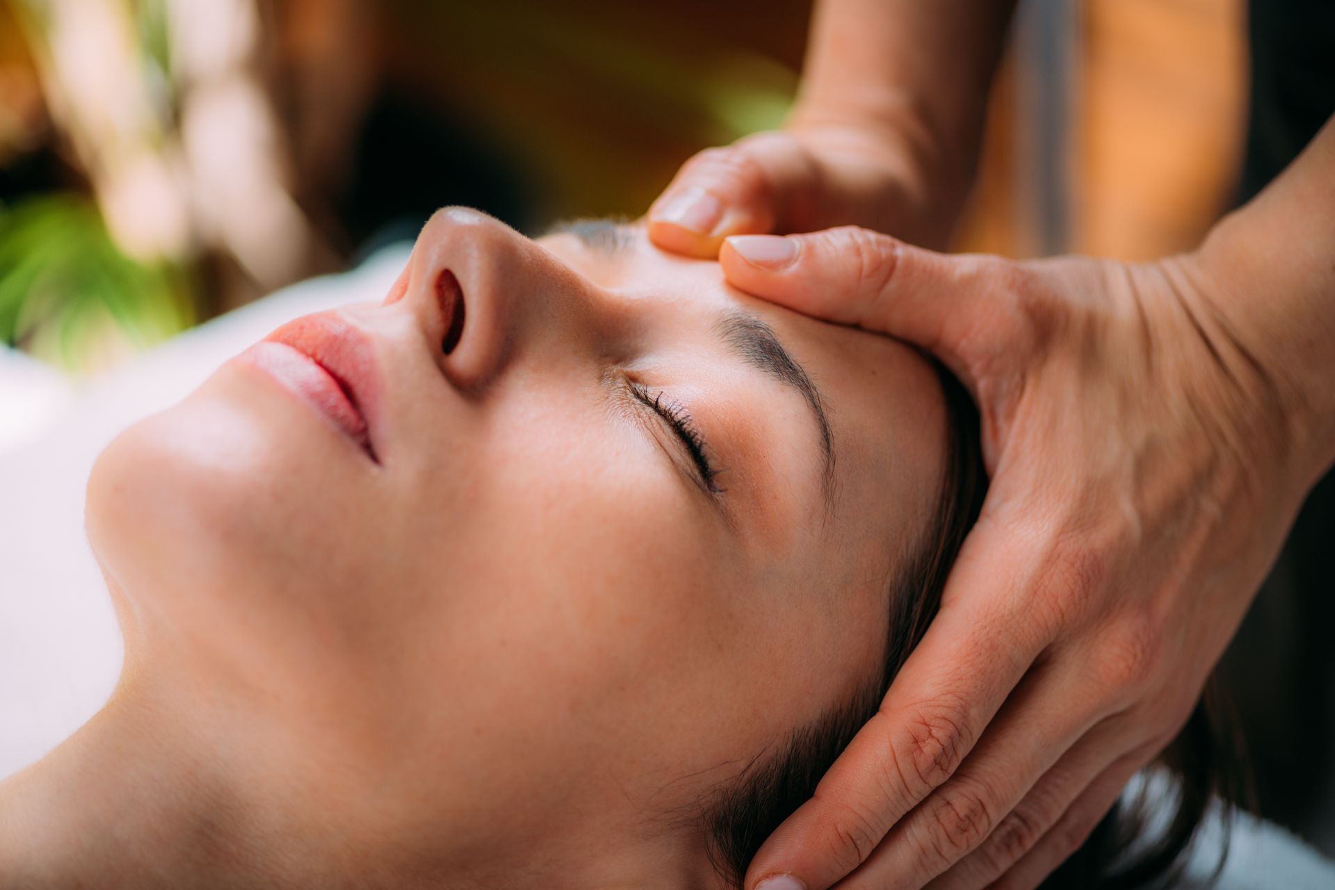 Woman receiving a gentle facial massage with eyes closed in a spa setting