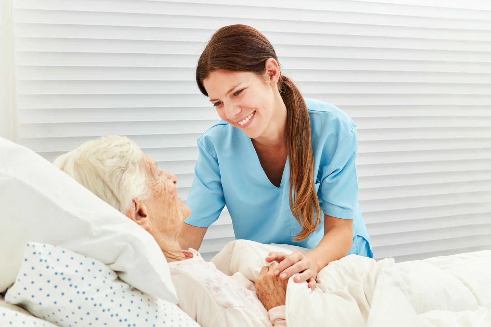 A nurse is talking to an elderly woman in a hospital bed.