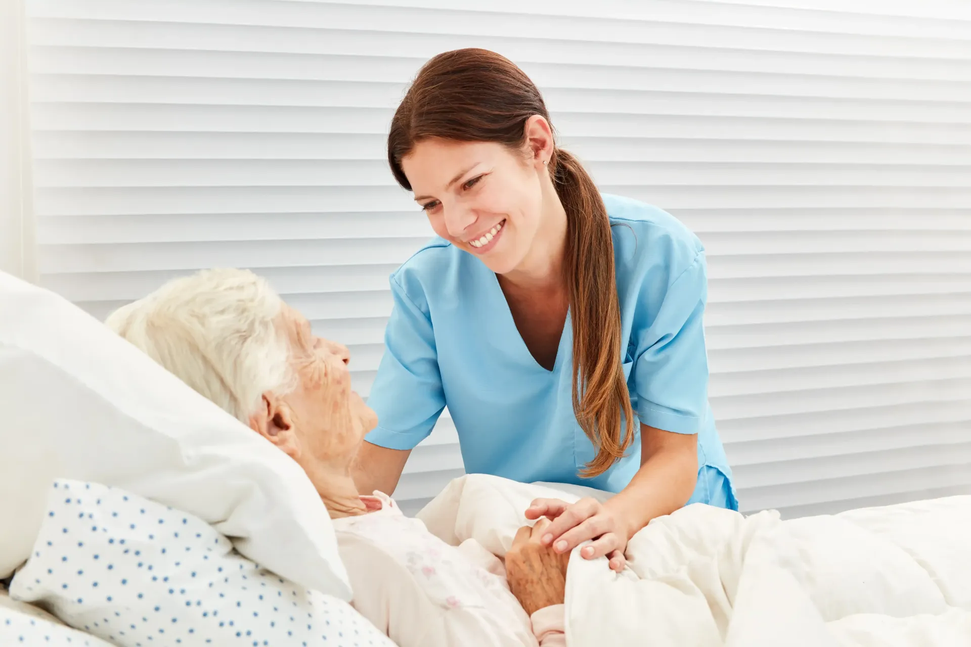 A nurse is talking to an elderly woman in a hospital bed.
