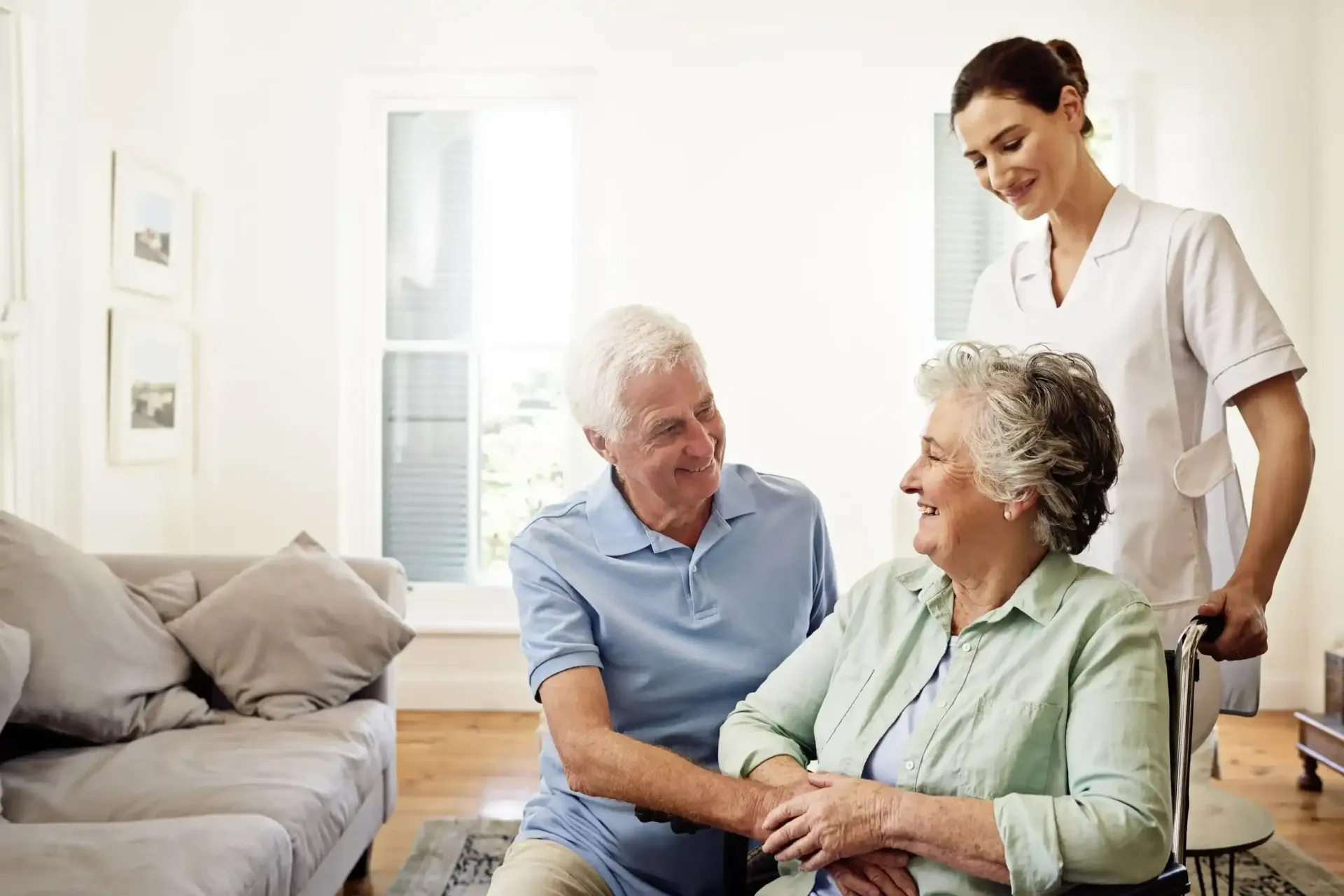 An elderly couple and a nurse are sitting on a couch in a living room.
