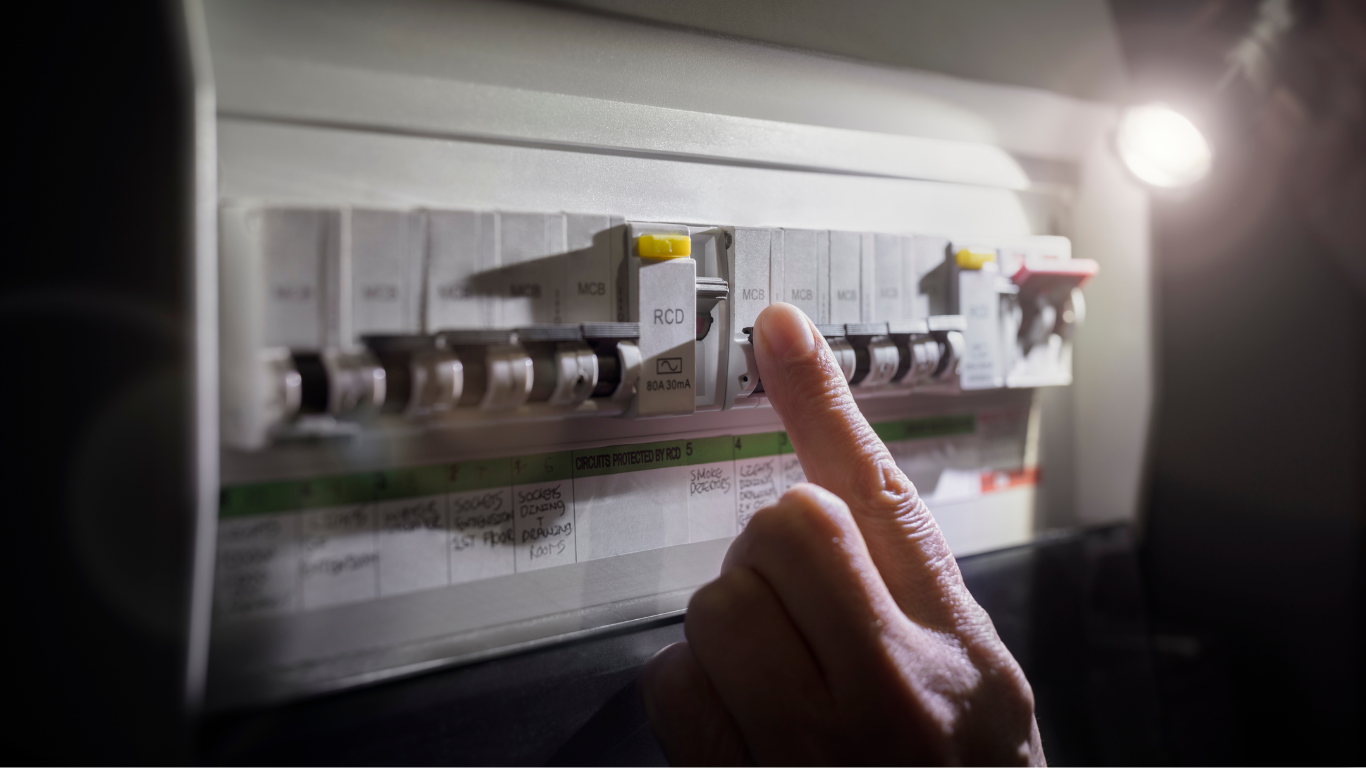 Technician testing wall wiring with a yellow multimeter at an electrical panel