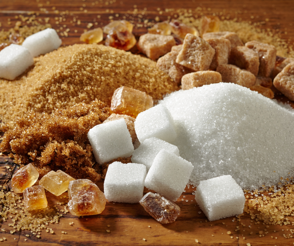 Various types of sugar: white granules, brown granules, brown cubes, white cubes, and crystal-like chunks, on a wooden surface.