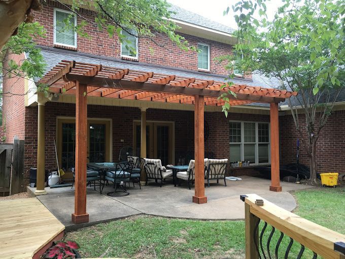 There is a wooden pergola in the backyard of a brick house.