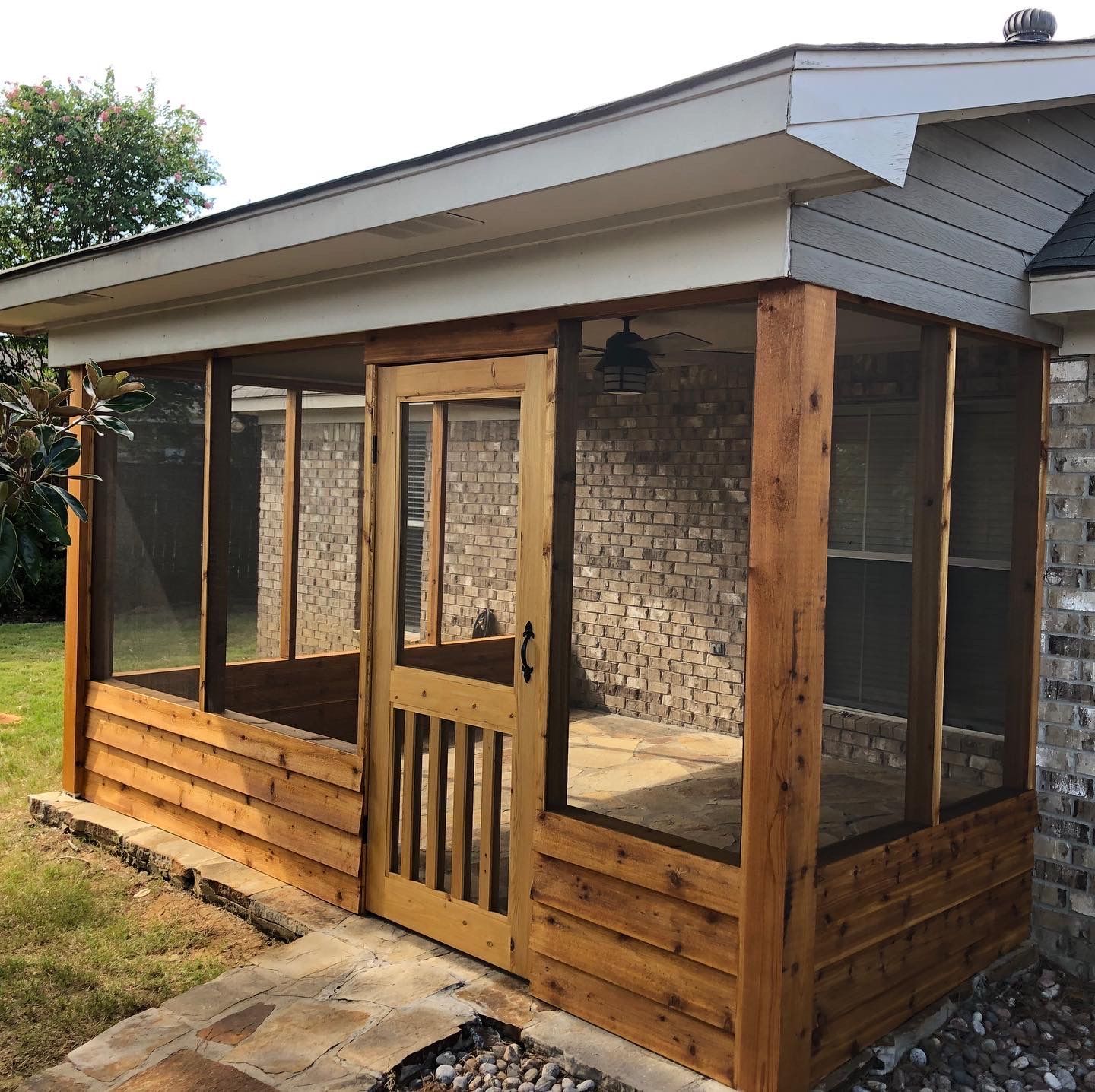A screened in porch with a brick house in the background.
