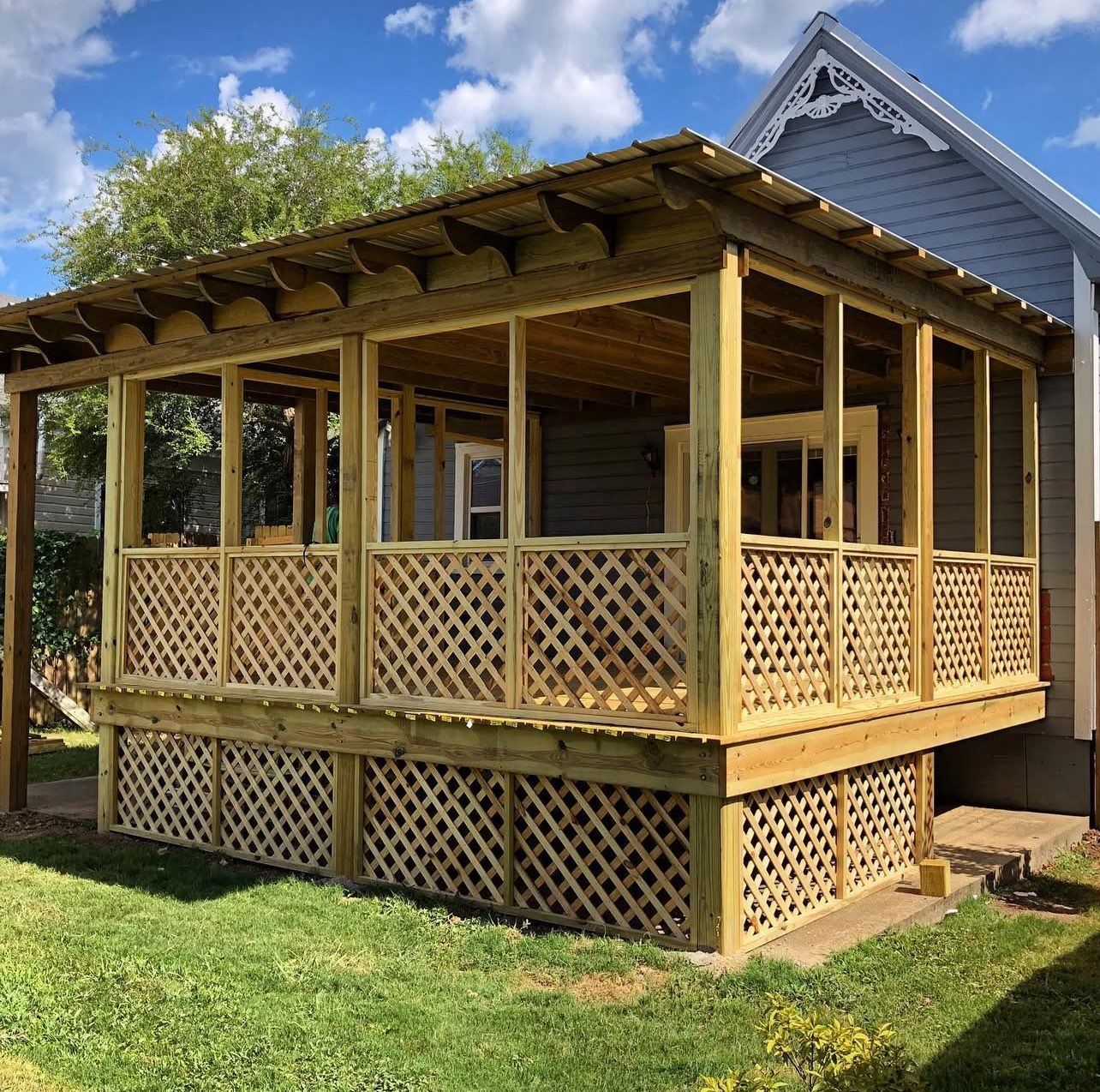 A wooden porch with a lattice railing is in front of a house.