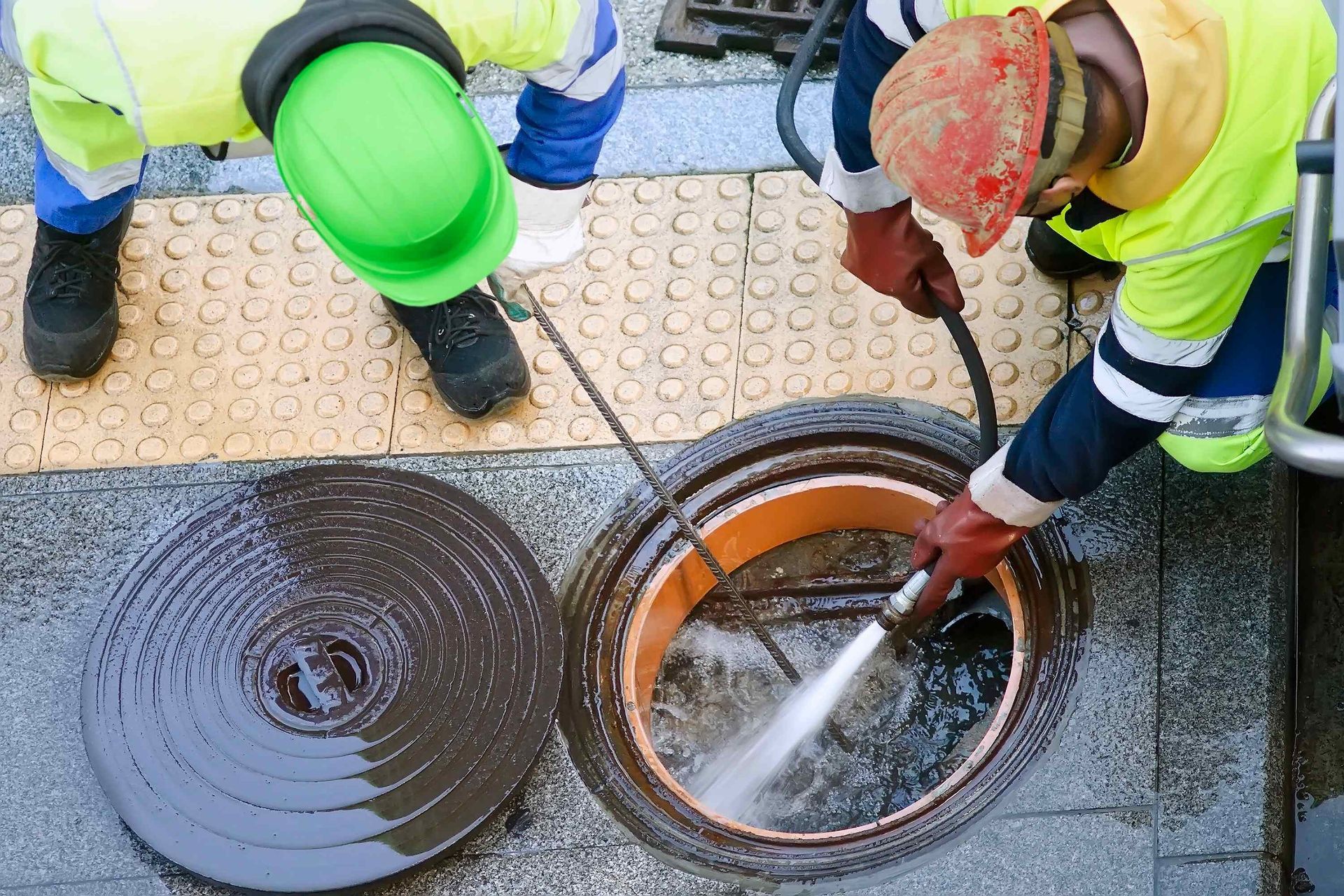 two men are cleaning a manhole cover with a high pressure washer