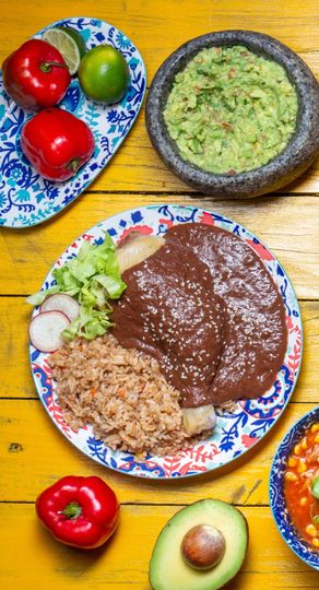 A plate of food with guacamole and rice on a wooden table.