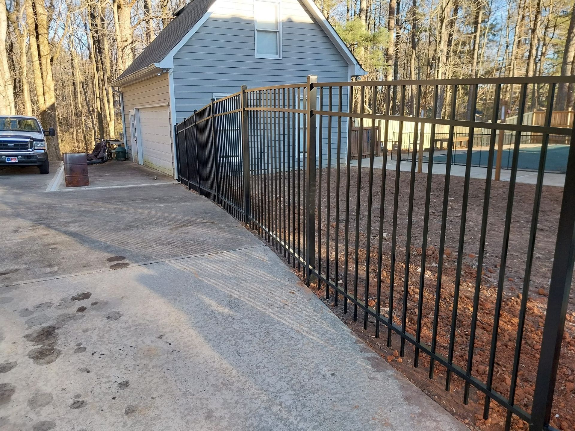 A black metal fence is surrounding a house in the woods.