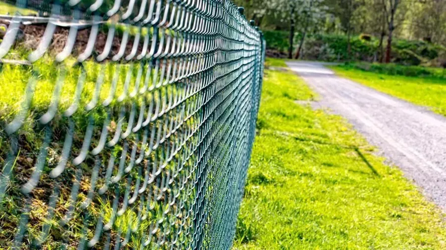 A chain link fence along a dirt road in a park.