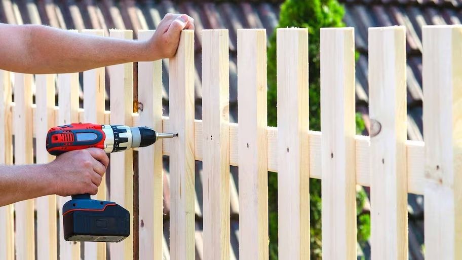 A person is using a drill to install a wooden fence.