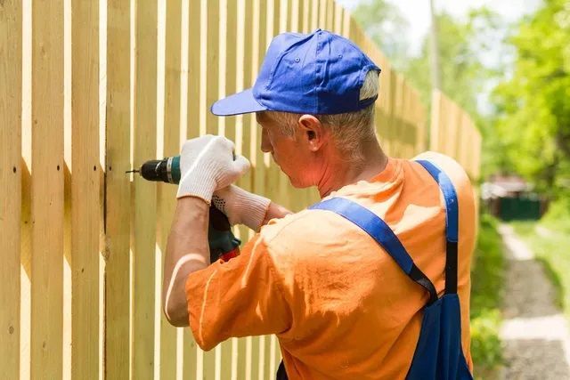 a man is using a drill to fix a wooden fence .