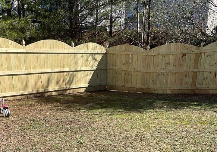 A new wooden scalloped-top privacy fence installed in a grassy backyard, with a small toy vehicle in the corner.