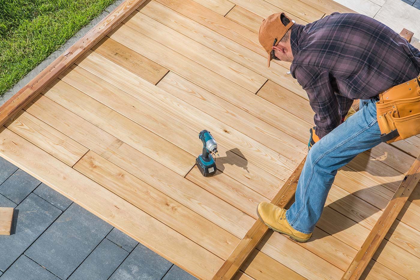 A man is working on a wooden deck with a drill .