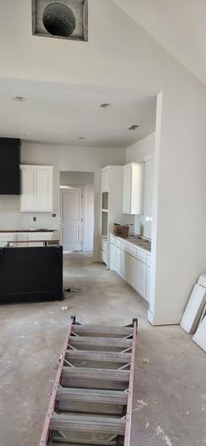 Kitchen under construction with white cabinets, black island, ladder, and unfinished floors.
