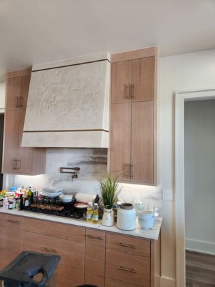 Kitchen with light wood cabinets, marble backsplash, range hood, and appliances.