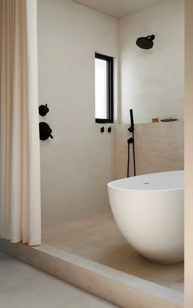 Modern bathroom with white oval tub, black fixtures, neutral walls, and a small window.