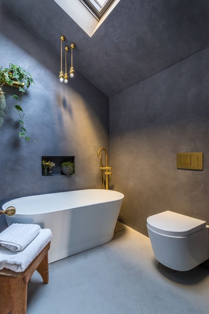 Modern bathroom with grey walls, white tub, brass fixtures, and skylight.