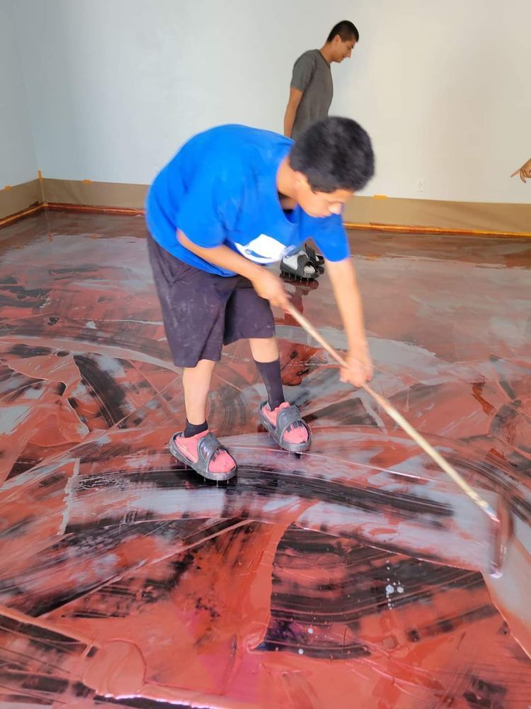 A person spreading red and black epoxy on a garage floor with a long handled tool.