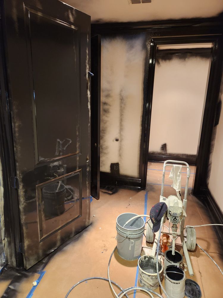 Room being painted with black paint, visible door frames and equipment.