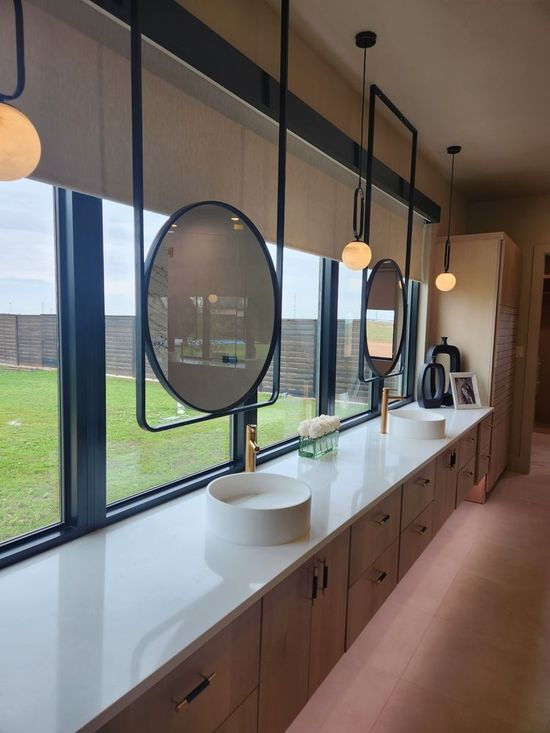 A long, modern bathroom with three sinks, mirrors, and window views of a backyard.