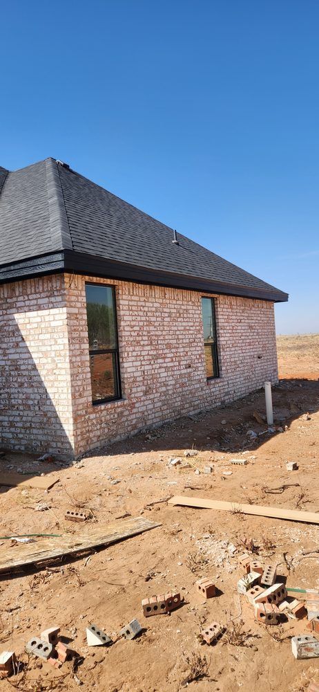 Brick house under construction with dark roof, clear blue sky.