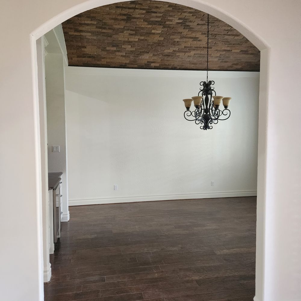 An arched doorway frames a room with a chandelier, wood ceiling, and dark wood floors.