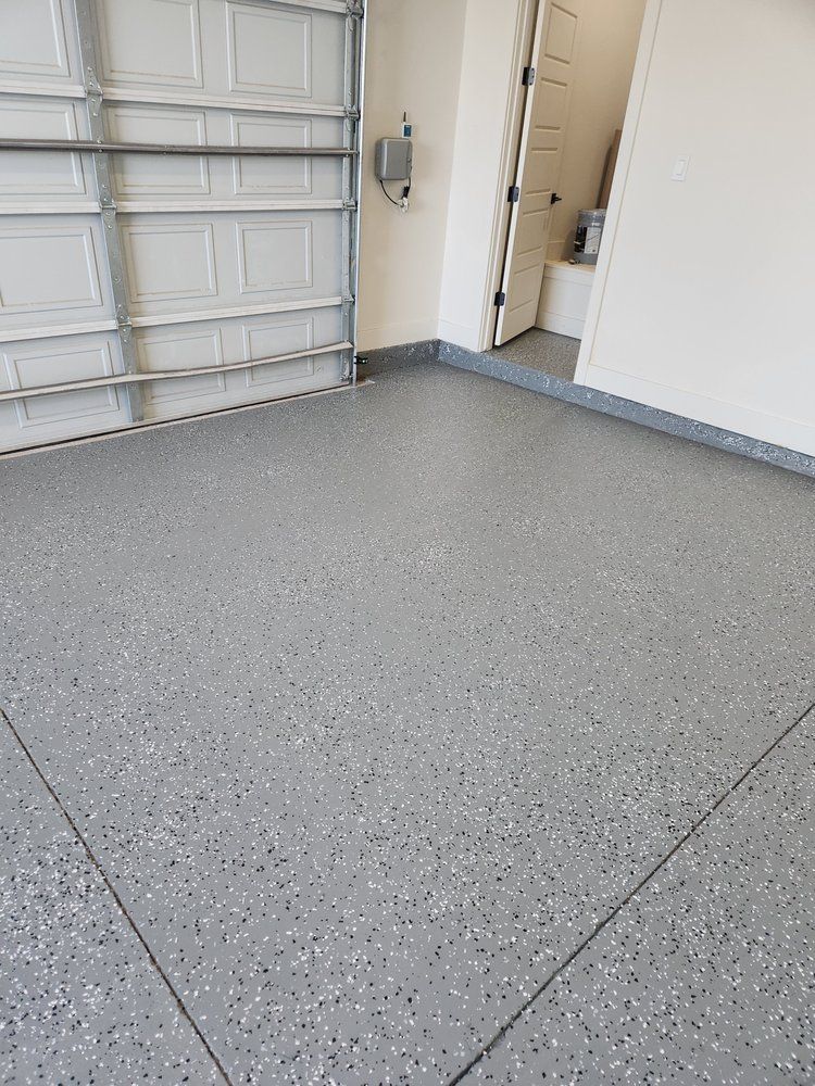 Gray speckled epoxy garage floor. Garage door and a white door are visible.