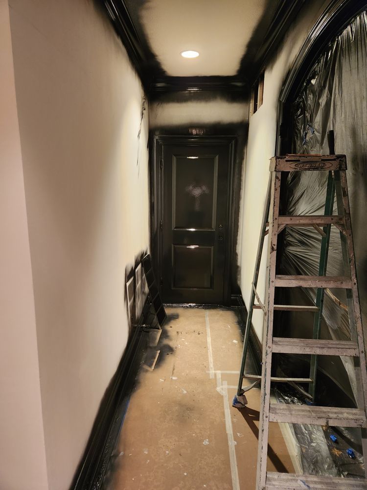 A hallway with black trim being painted; a wooden ladder rests against the wall.