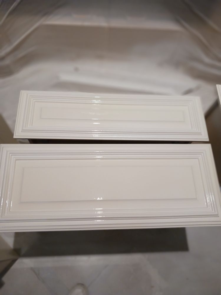 Two white cabinet doors with a glossy finish sit on a protective surface.