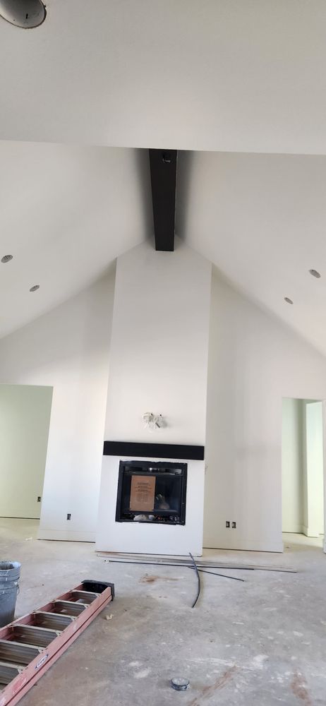 White interior with fireplace and black beam. Construction in progress.