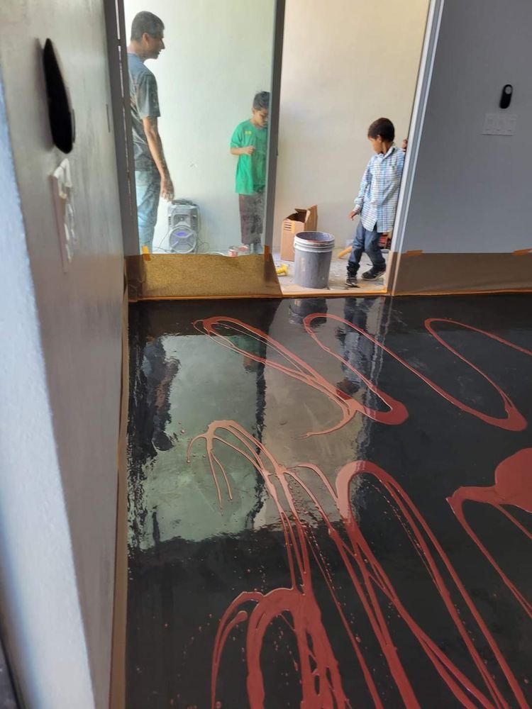 People in a room with a partially painted floor; red paint swirls on a dark surface, children in the doorway.