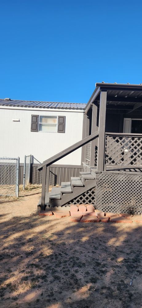 A wooden porch with stairs next to a white house with black shutters on a clear, blue sky day.