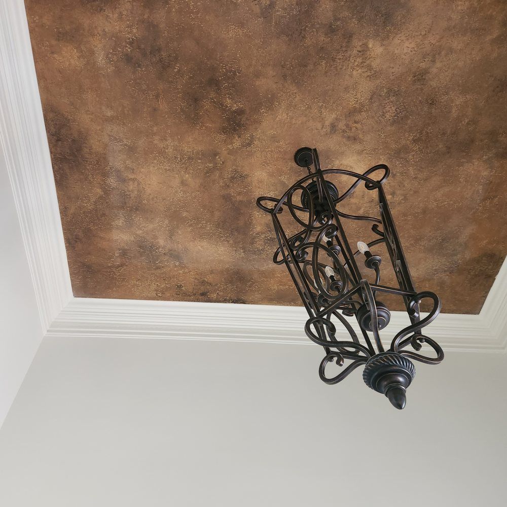 Chandelier hangs below a brown, textured ceiling framed by white molding. White walls form the room.