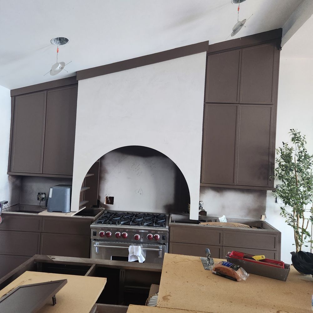 Kitchen under renovation; brown cabinets, white range hood, gas stove, exposed construction.