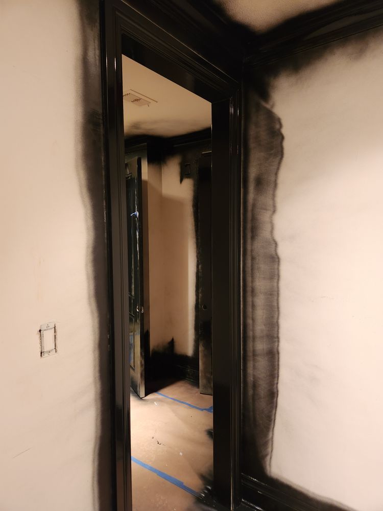 A dark doorway with black trim, partially painted; light-colored walls and floor, interior hallway.