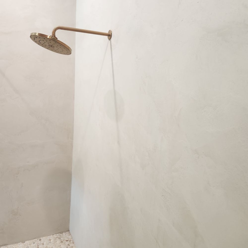 Gold showerhead attached to a light-colored wall.