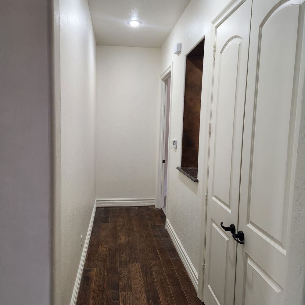 Narrow hallway with wood flooring, white walls, and a recessed shelf. A door is on the right.