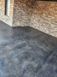 Dark stained concrete patio with brick walls and a window.
