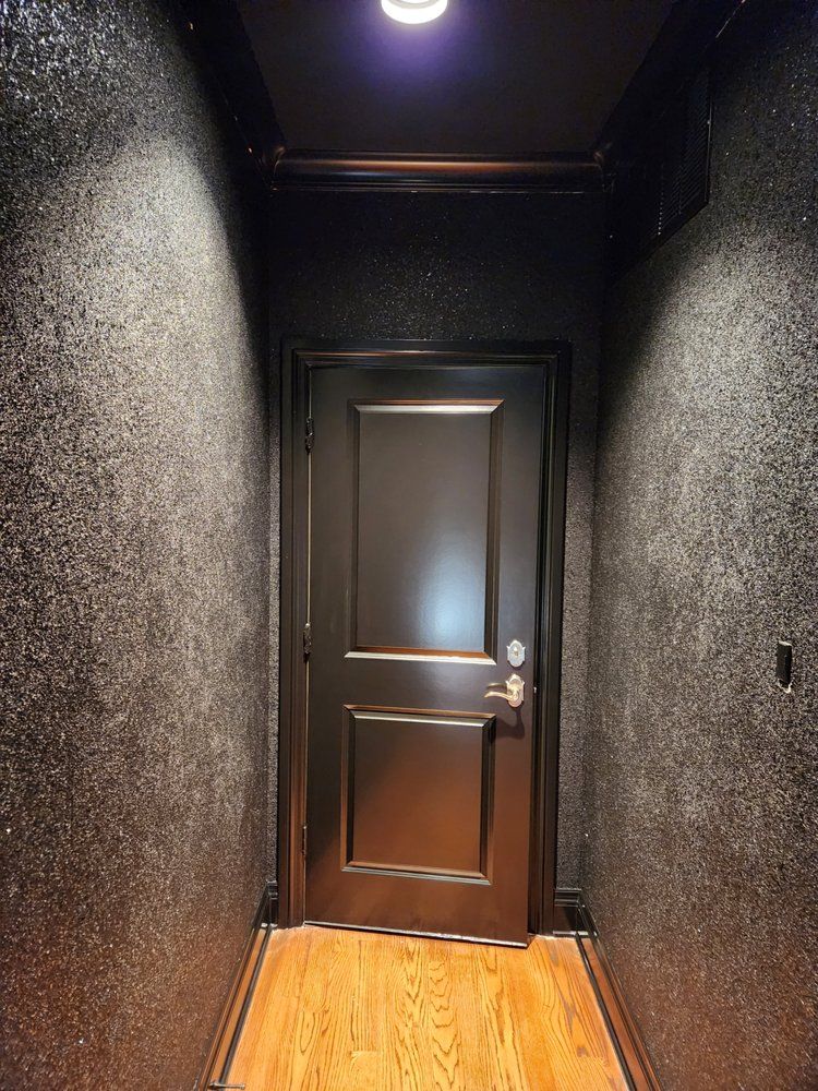 Dark hallway with black door and speckled walls, lit by a ceiling light and spotlights.