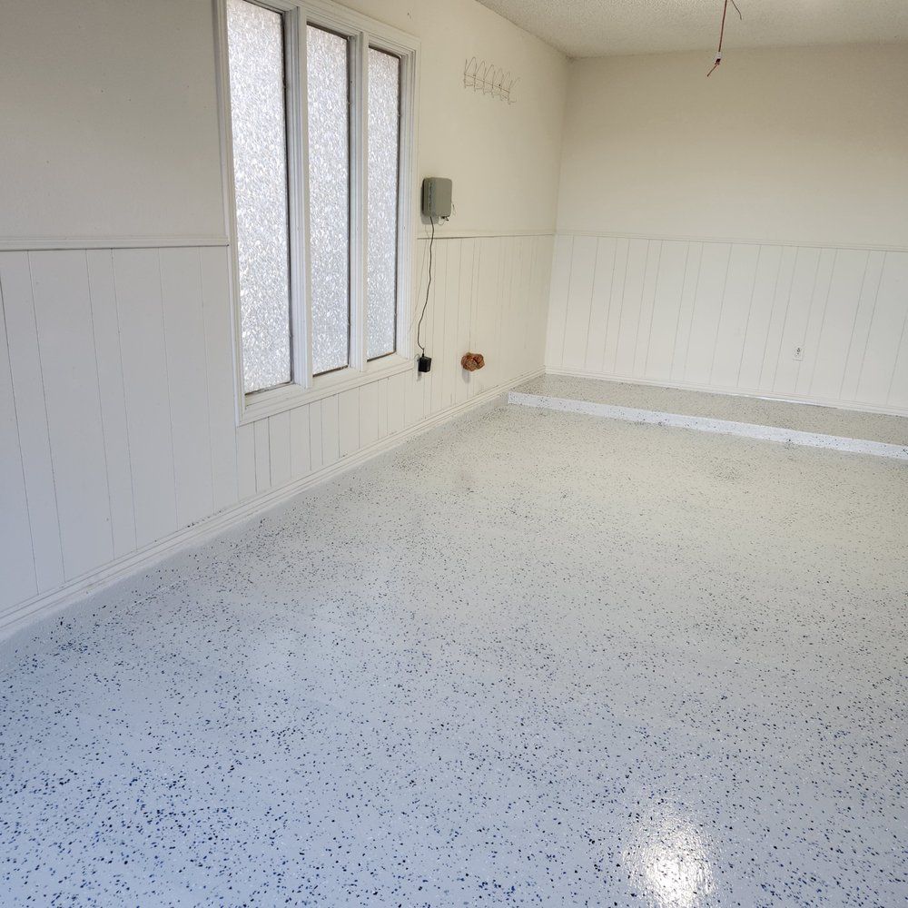 Empty white room with speckled floor, window, and white wainscoting.