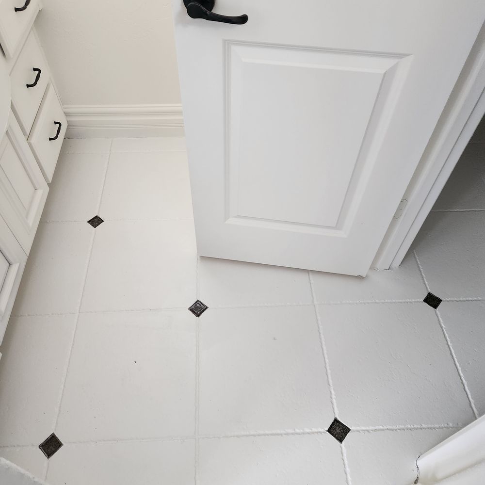 White tile floor with black diamond accents, white door and cabinet.