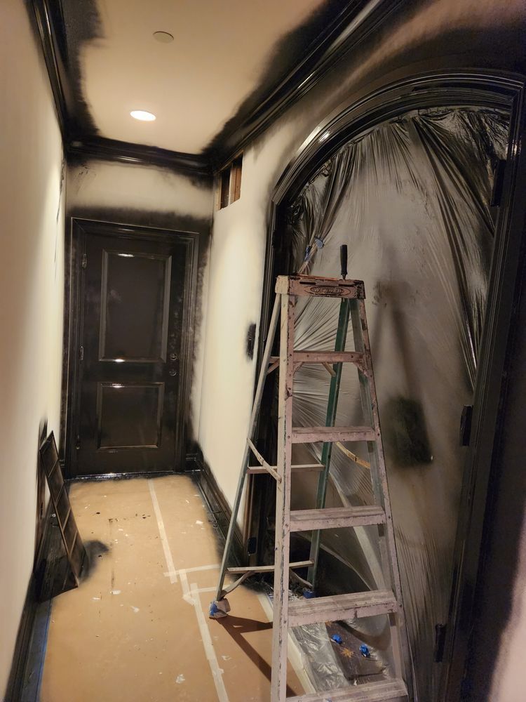 Hallway being painted black; a ladder stands near an arched doorway; walls are white, floor covered.