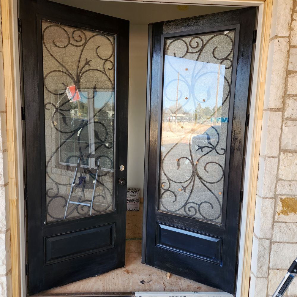 Black double doors with glass panels and ornate ironwork; beige stone wall background.