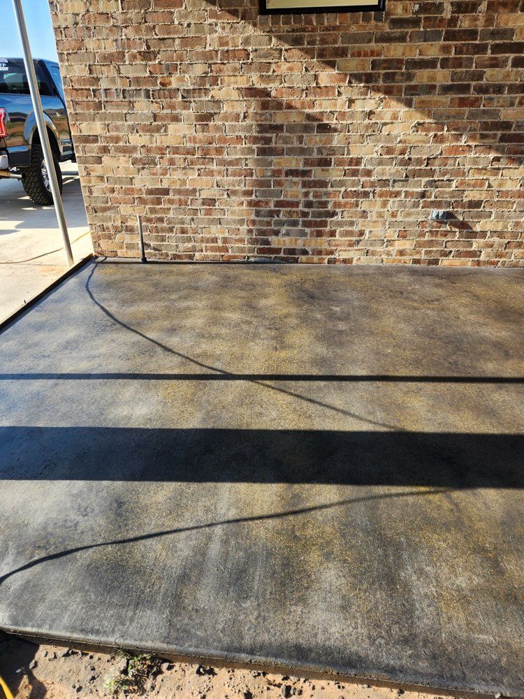 A dark brown and yellow concrete patio against a brick wall, with long shadows.