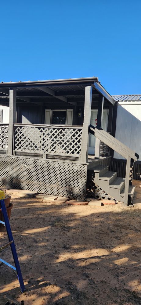Gray painted porch with lattice railing, steps, and overhead roof on a house; clear blue sky.