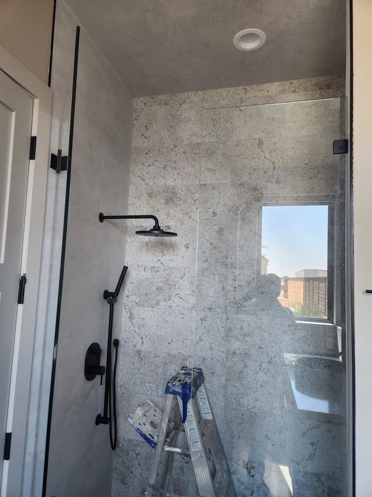 Black shower fixture in a gray tile shower with a glass door; stepladder inside.