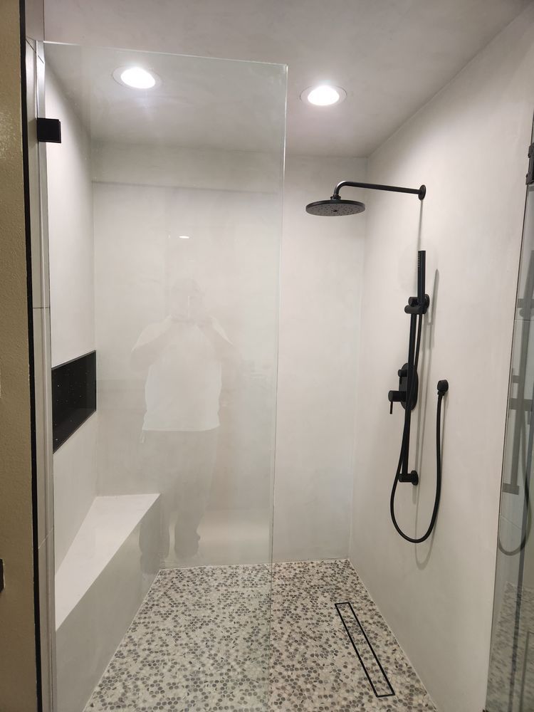 Modern white and black shower with a glass panel, bench, and showerhead.