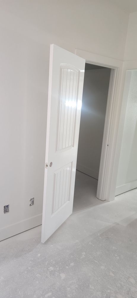 White door in a light-colored room with unfinished flooring and plain white walls.