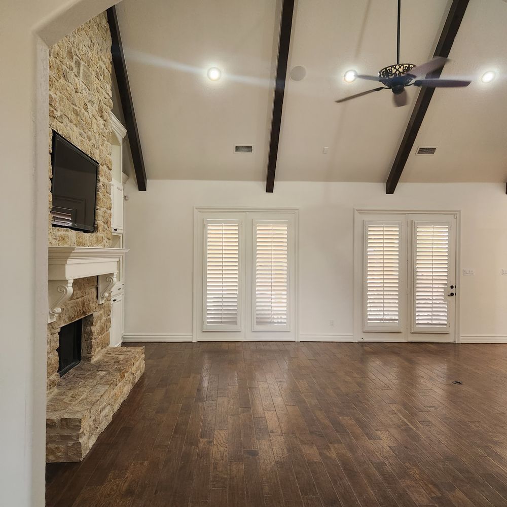 Living room with stone fireplace, dark wood floors, white walls, and shuttered doors.
