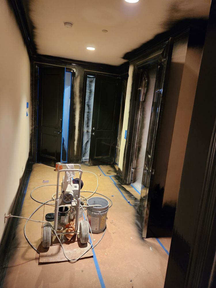 Hallway being painted black, masking tape protects walls and trim. Paint sprayer and supplies are present.